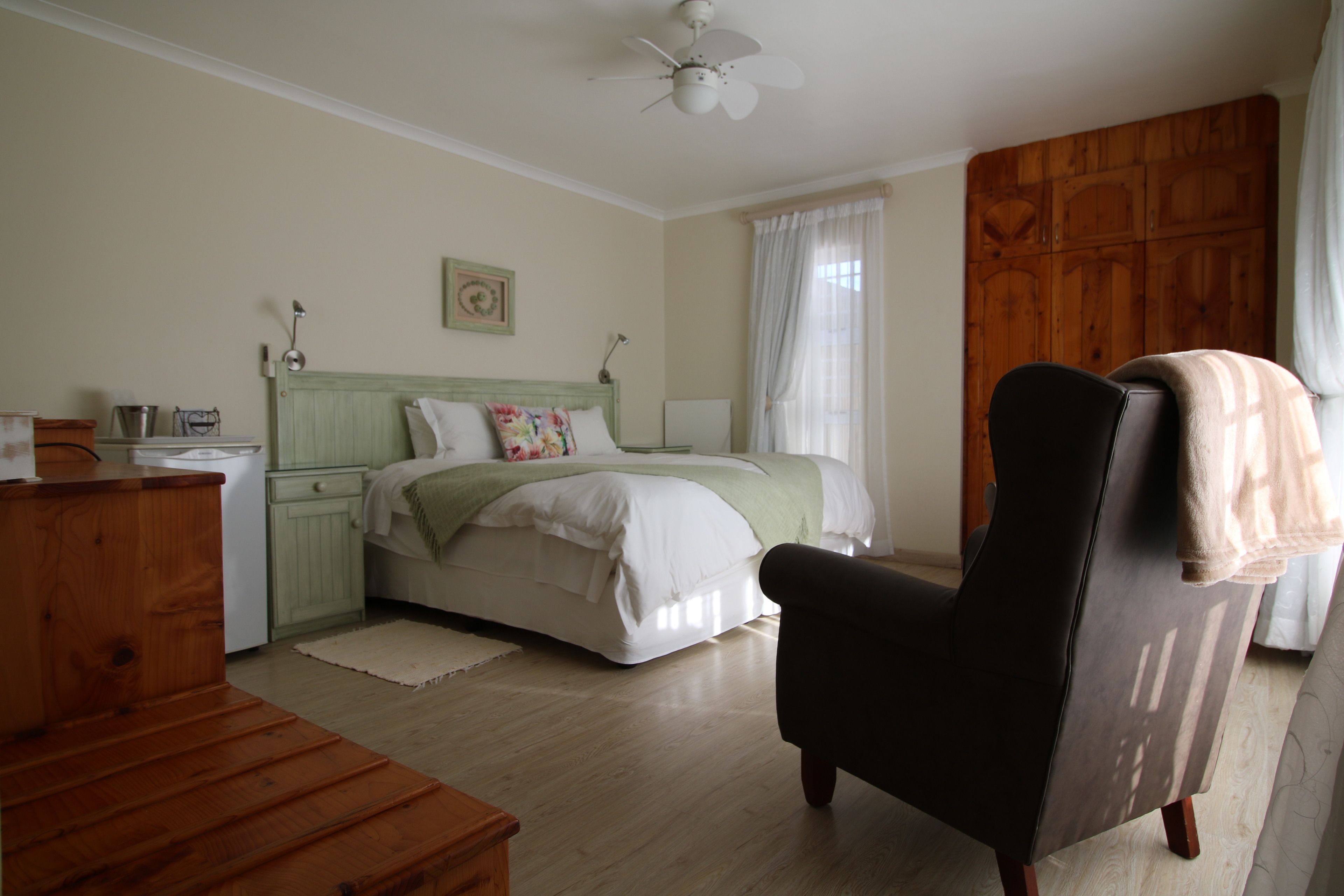 A bedroom with a bed, a wooden chair, a dresser, and a ceiling fan.