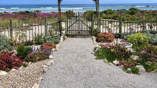 A pathway leading to a wooden archway with a view of the ocean.