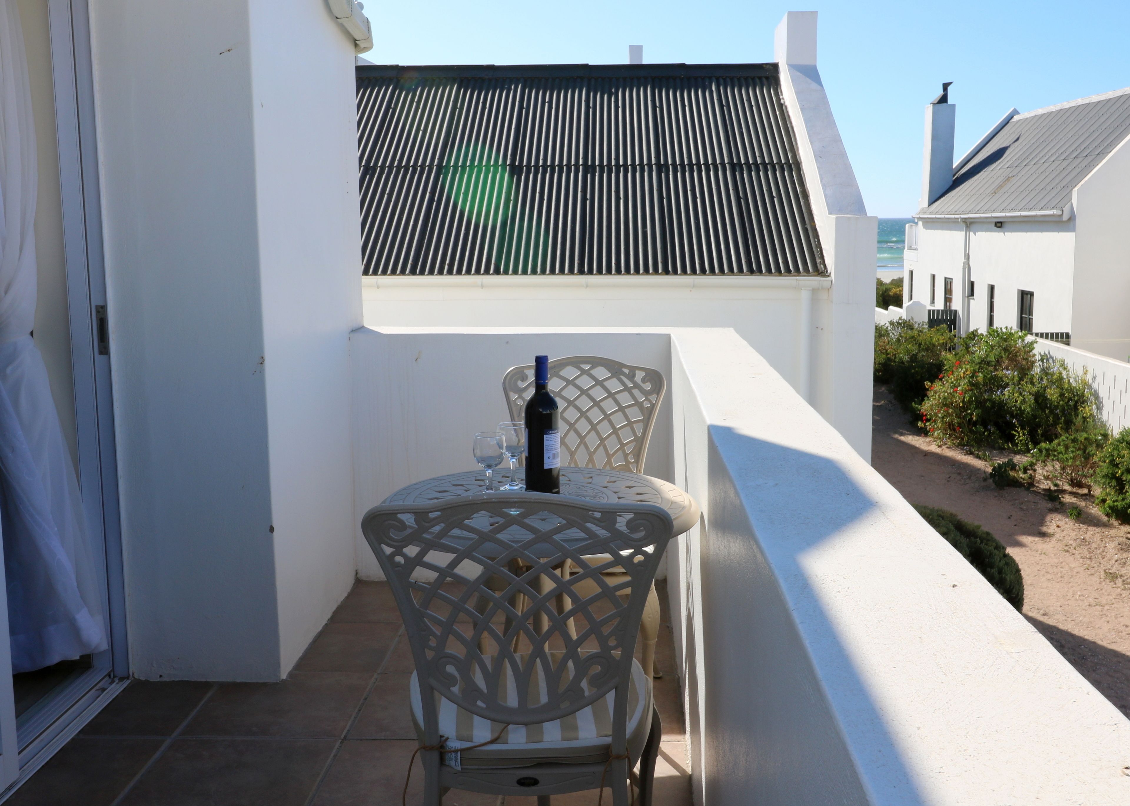Een balkon met een tafel en stoelen, een fles wijn en uitzicht op zee.