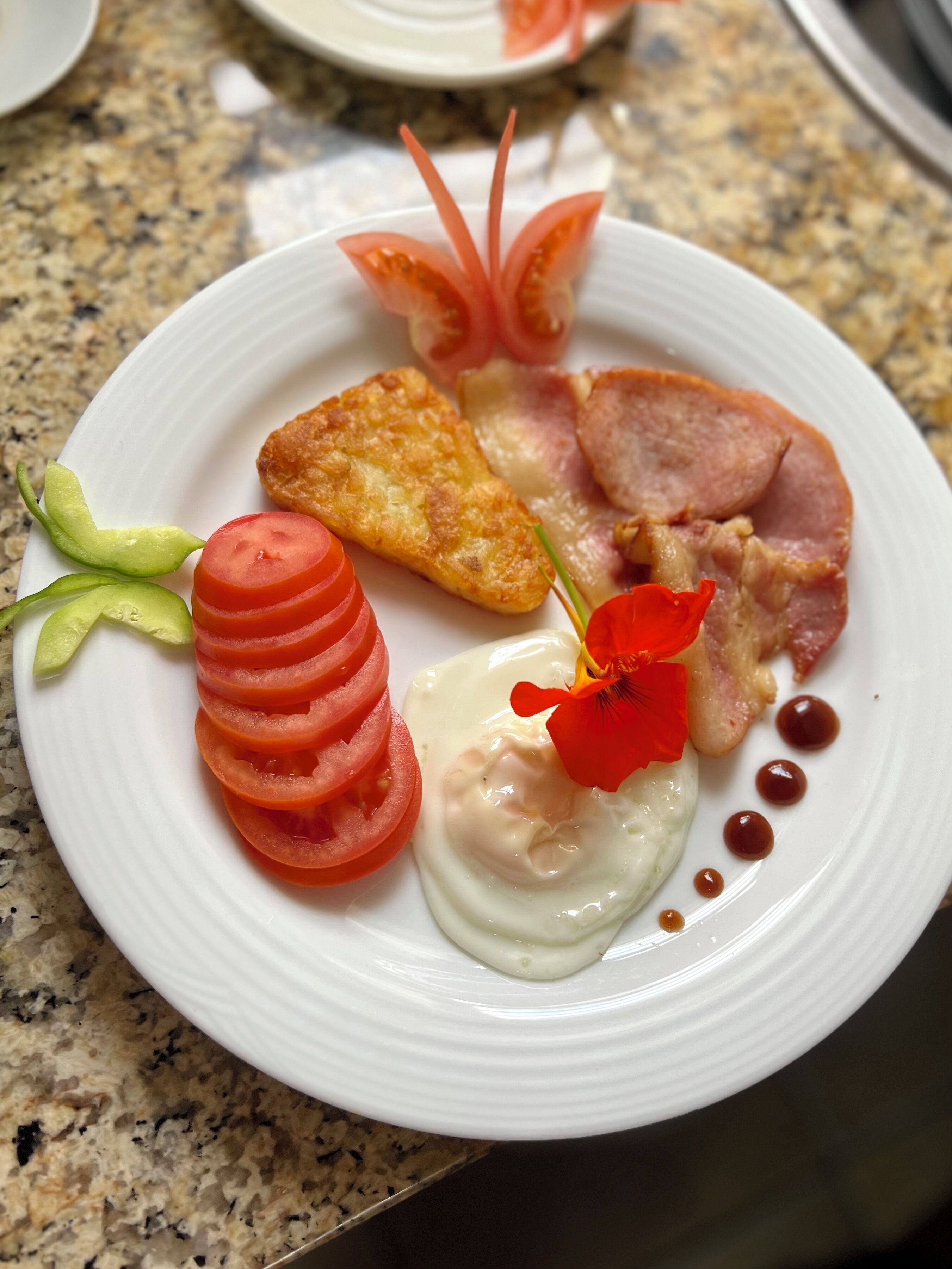 A white plate with a variety of food items including sliced tomatoes, a fried item, and a piece of meat, arranged on a granite countertop.