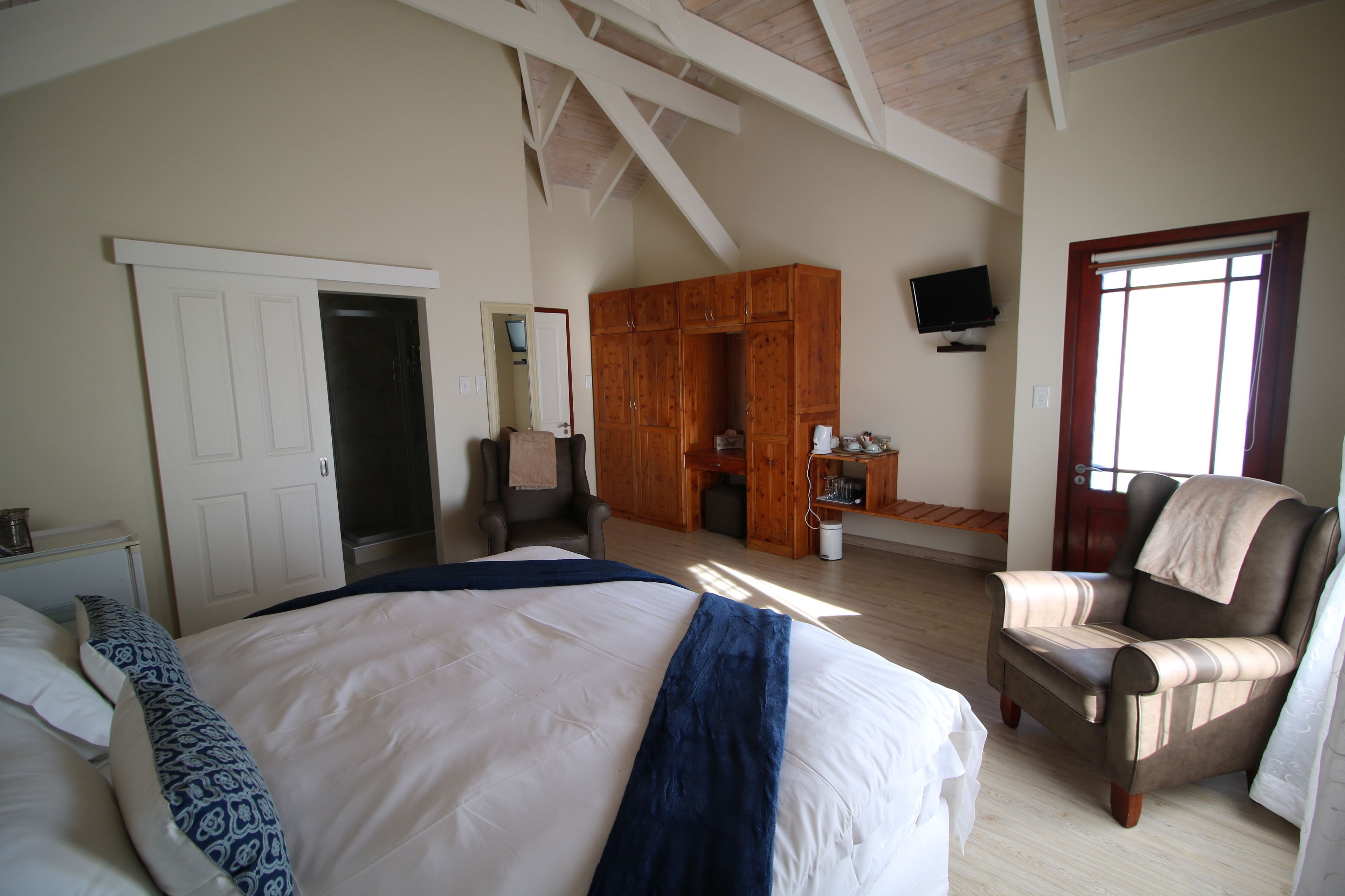 A bedroom with a large bed, a wooden wardrobe, a chair, and a television on the wall.