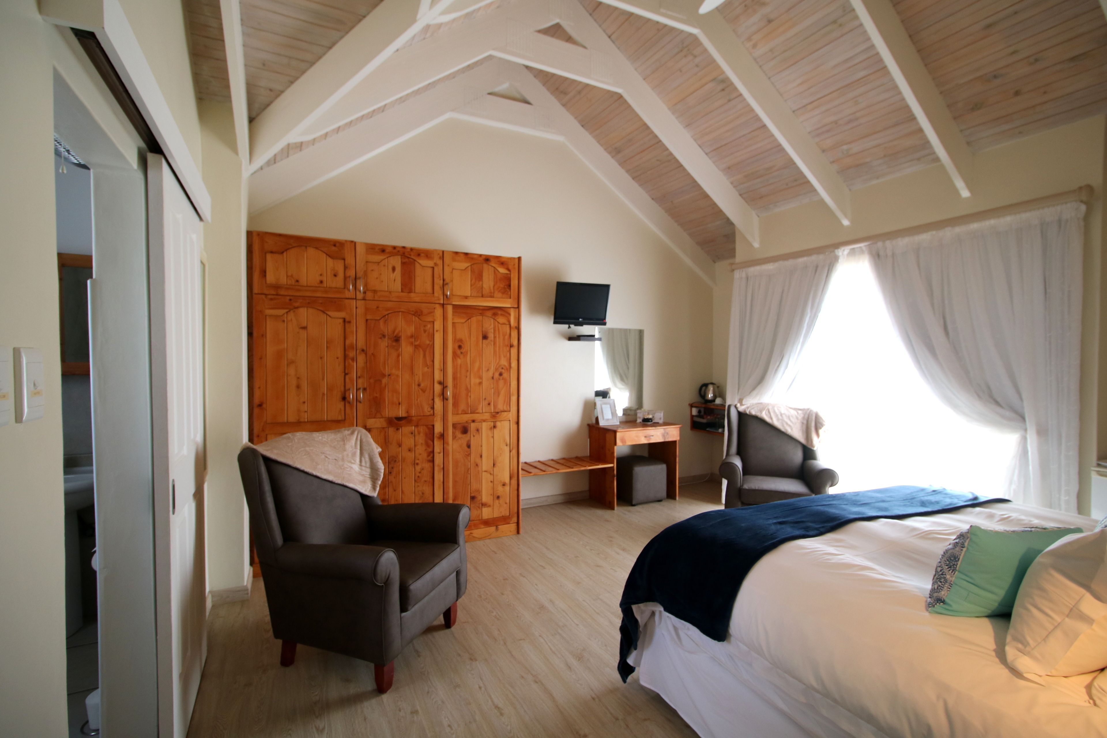 A bedroom with a bed, a desk, a chair, a wardrobe, and a television.