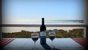 A table with a bottle of wine and two glasses, overlooking a beach and ocean view.