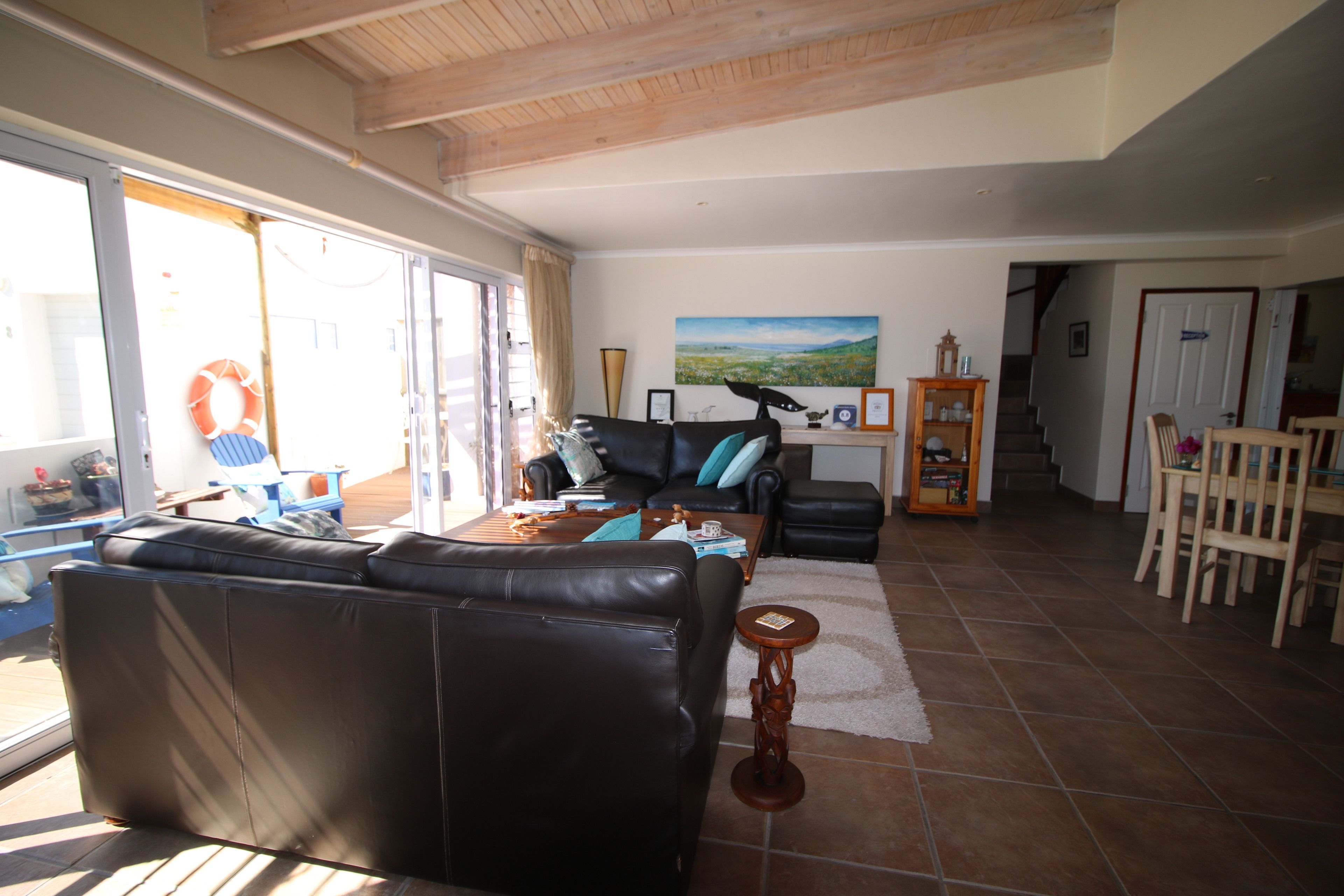 A spacious living area with a large leather sofa, a coffee table, and a dining table with chairs. There is a painting on the wall and a wooden cabinet.