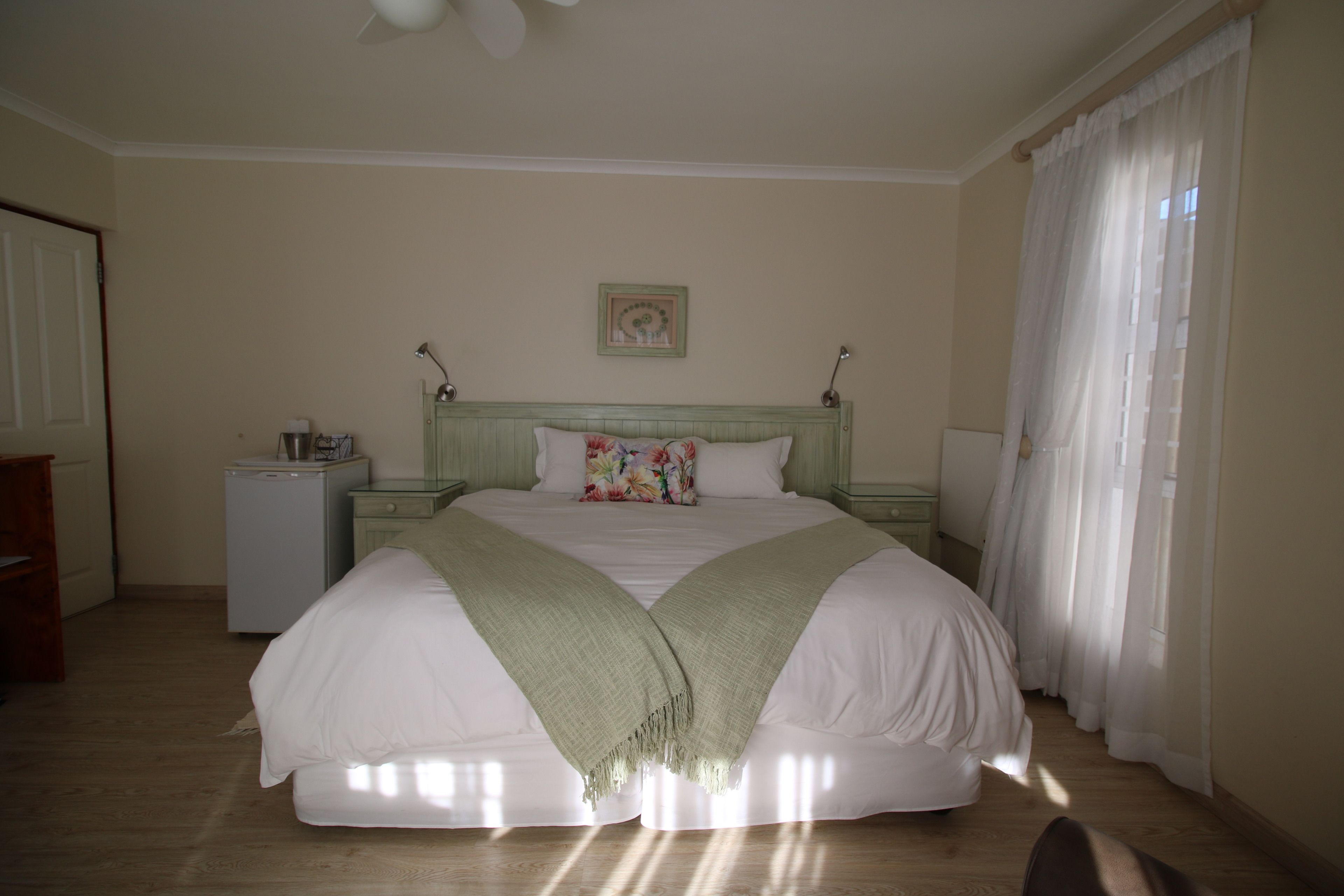 A bedroom with a bed, bedside tables, a nightstand, a lamp, a picture on the wall, and a window with curtains.