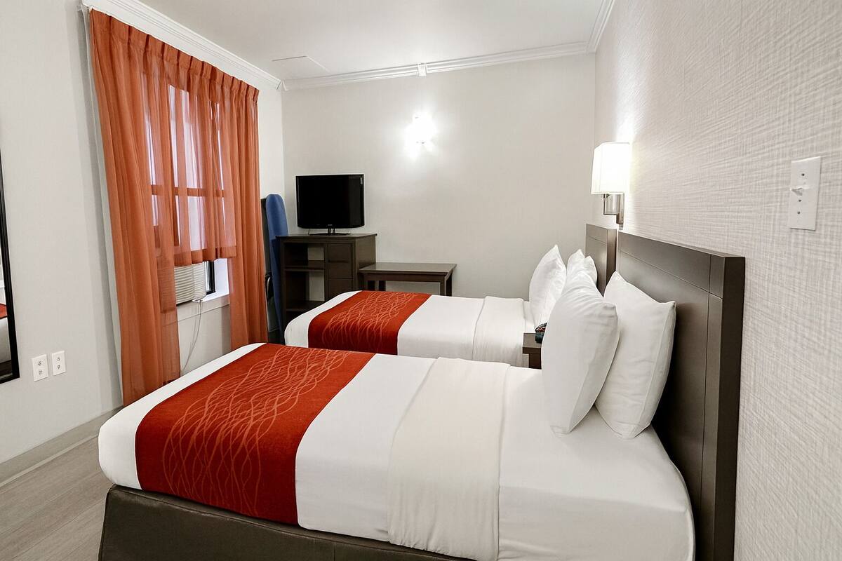 Ein Hotelzimmer mit zwei Betten, einem Fernseher, einem Schreibtisch und einer Lampe.