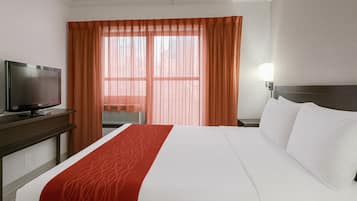 A hotel room with a bed, a TV, a nightstand, and a window with curtains.