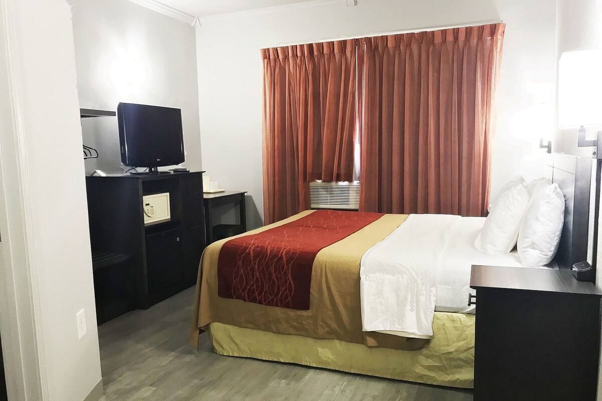 Ein Hotelzimmer mit einem Bett, einem Schreibtisch mit Fernseher, einem Fenster mit Vorhängen und einem Wandheizgerät.