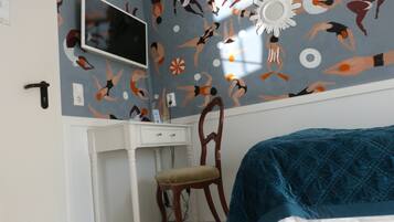 A bedroom with a bed, a desk, and a chair. The wall has a pattern of swimmers.
