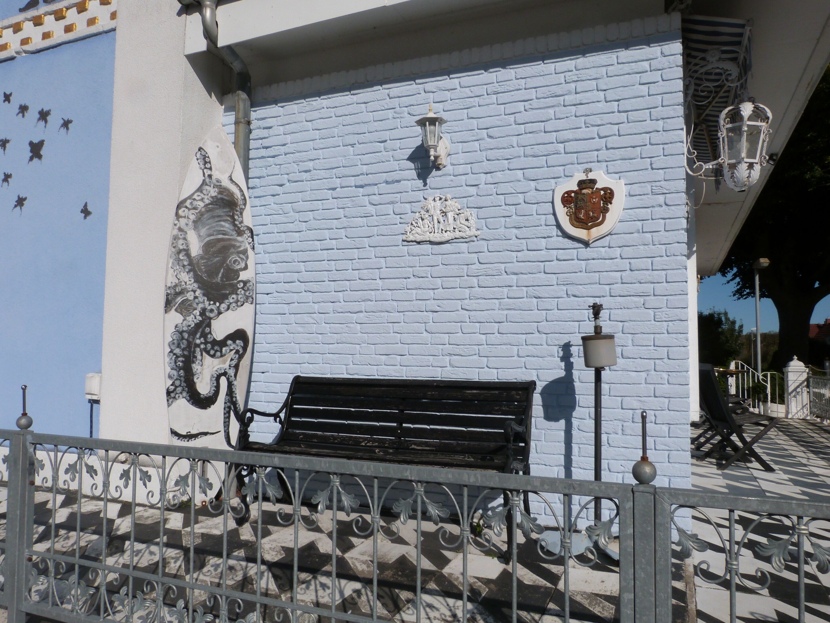 A bench against a wall with a mural, a coat of arms, and two wall-mounted lanterns.