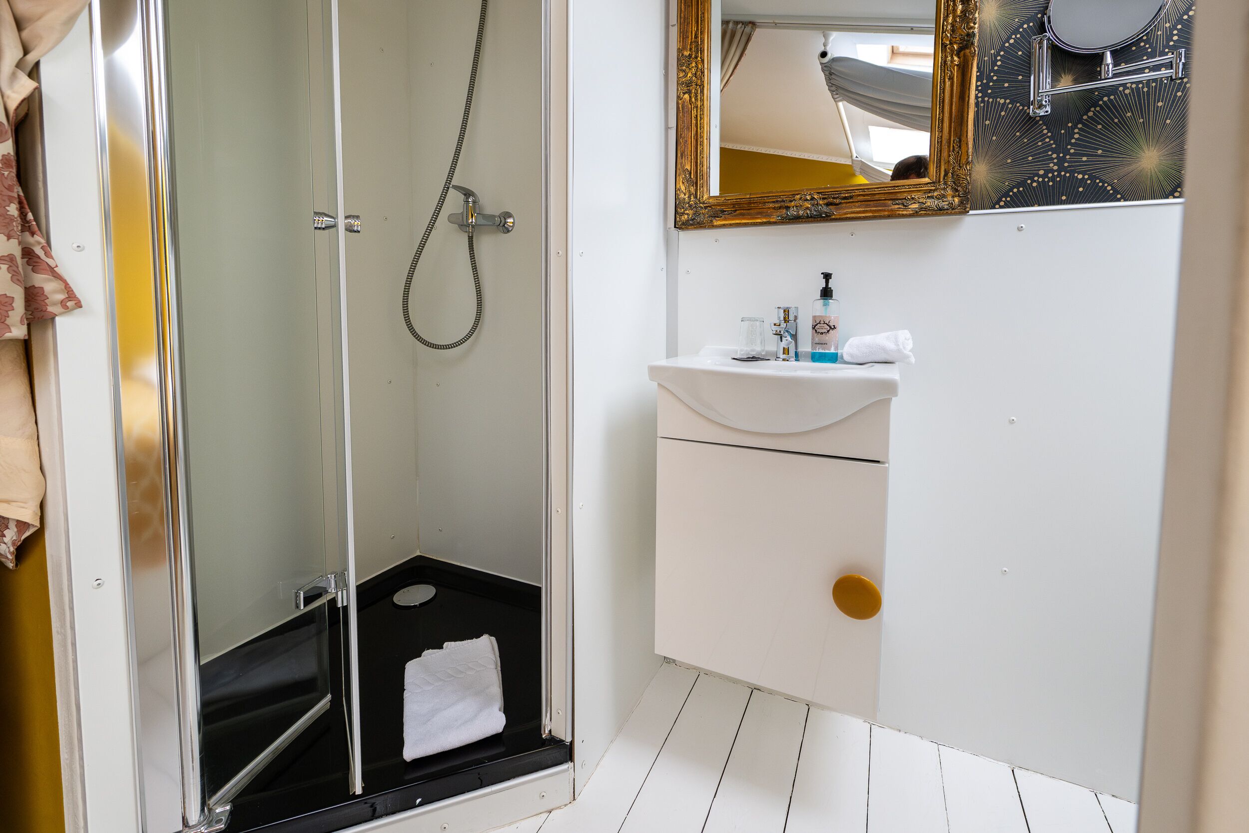 Un bany amb dutxa tancada amb vidre, un lavabo blanc i un mirall amb marc decoratiu.