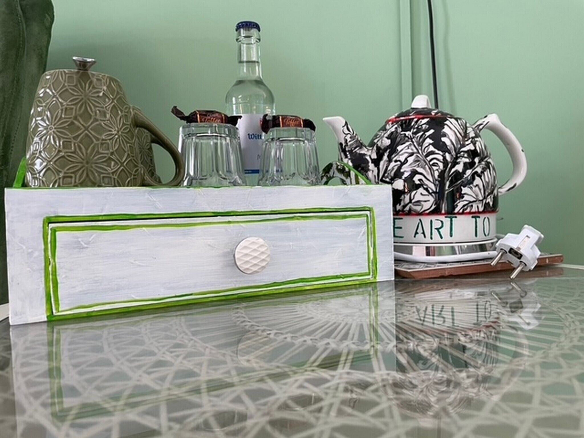 Une table agrémentée d’un plateau décoratif, d’un vase à motifs, d’une bouteille, d’une théière et d’une tasse ornée de motifs floraux.