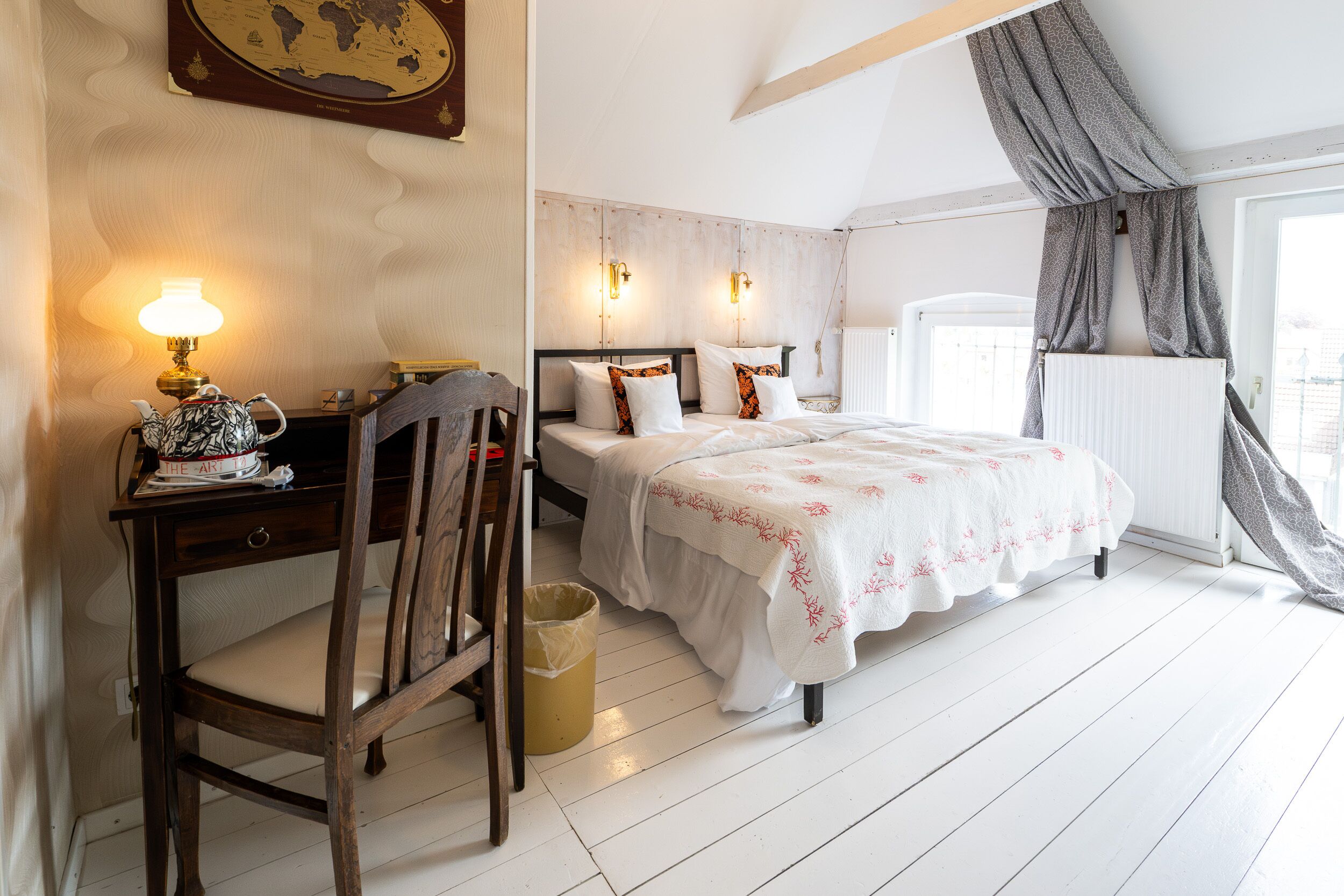 A bedroom with a bed, bedside tables, a desk with a lamp, a chair, and a window with curtains.