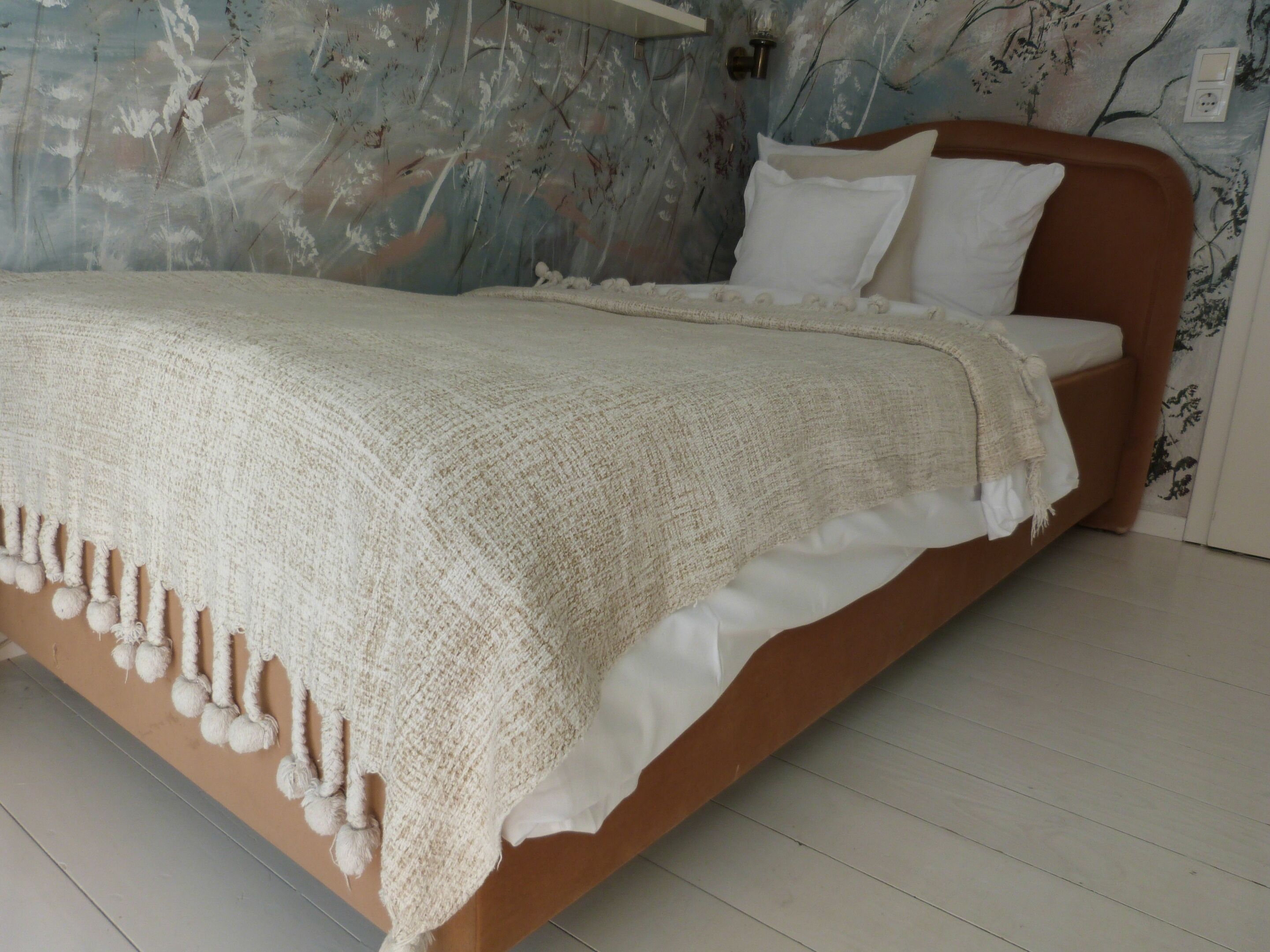 Un letto con coperta e cuscini bianchi, una testiera in legno e una parete con motivo floreale.