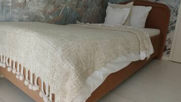 Un letto con coperta e cuscini bianchi, una testiera in legno e una parete con motivo floreale.