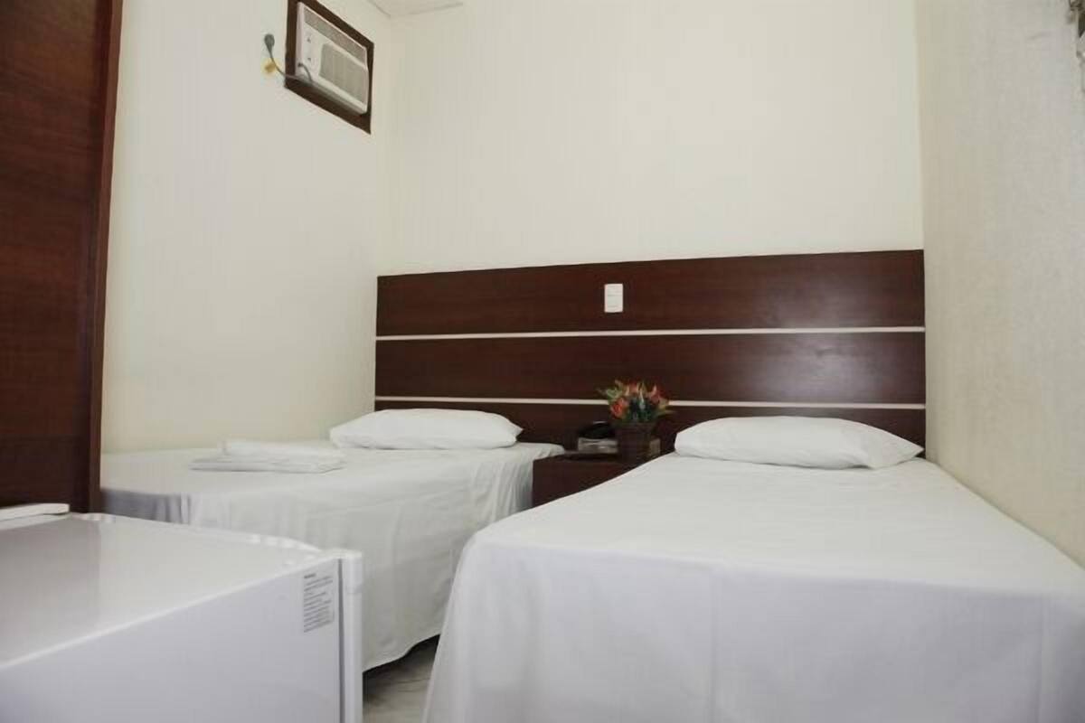 Una habitación de hotel con dos camas individuales, un cabecero de madera, una mesita de noche pequeña con una lámpara y un cuadro en la pared.