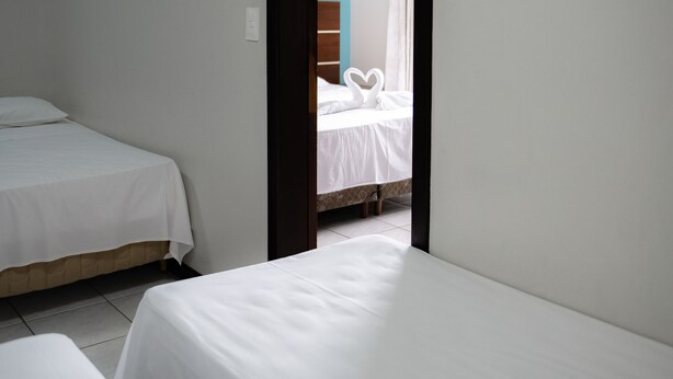 A room with two single beds, a wooden headboard, and a door leading to another room with a bed and a curtain. - Blu Terrace Hotel (Blumenau)