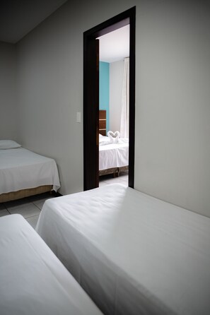 Una habitación con dos camas individuales, un cabecero de madera y una puerta que da a otra habitación con una cama y una cortina.