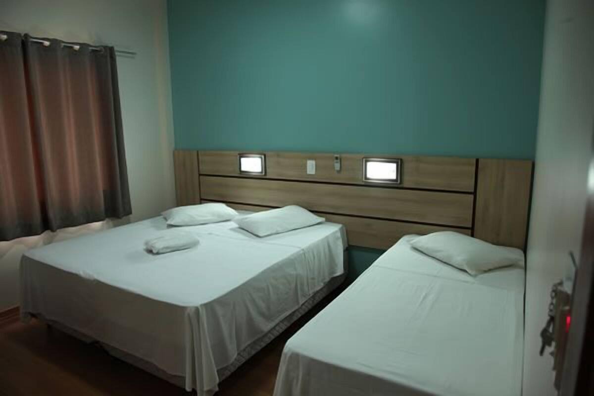 Habitación de hotel con dos camas individuales, cabecero de madera y pared color aguamarina.