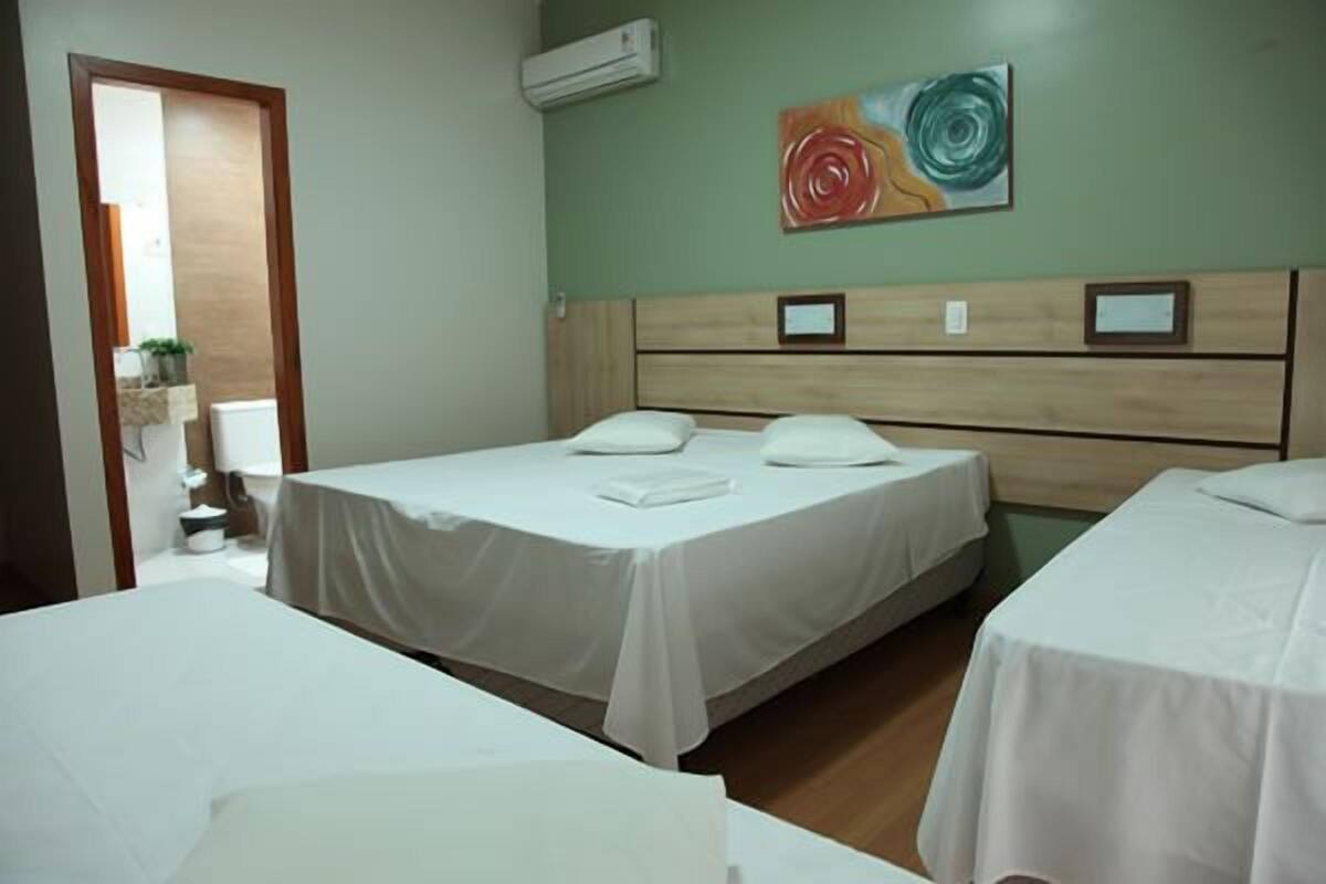 Habitación de hotel con dos camas, cabecero de madera, un cuadro en la pared y una planta pequeña en la mesita de noche.