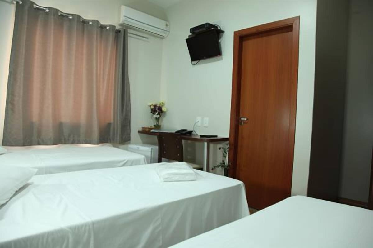 Habitación de hotel con dos camas, un escritorio con teléfono y una planta pequeña, una puerta de madera y un equipo de aire acondicionado en la pared.