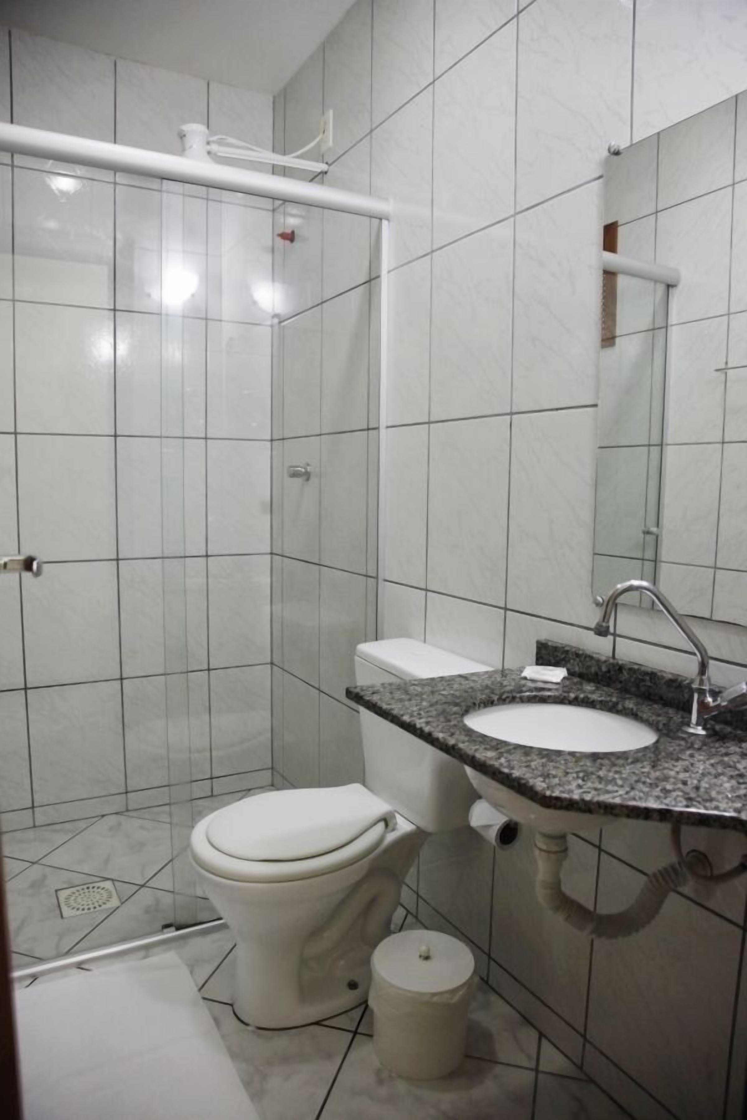 Un baño con azulejos blancos, un inodoro, un lavabo con encimera de granito y una zona de ducha.