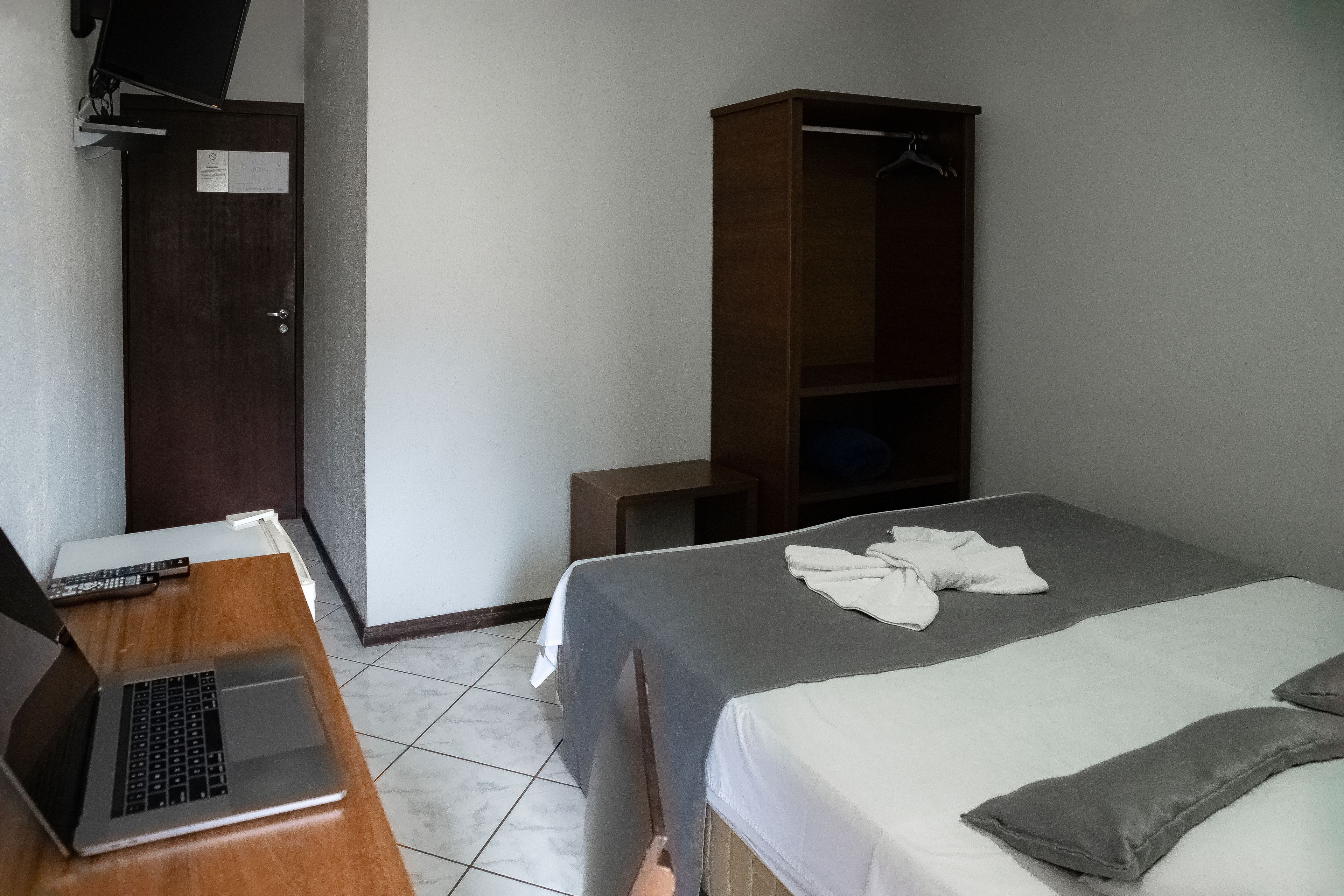 Habitación de hotel con cama, armario de madera, escritorio con una computadora portátil y puerta con un cartel.
