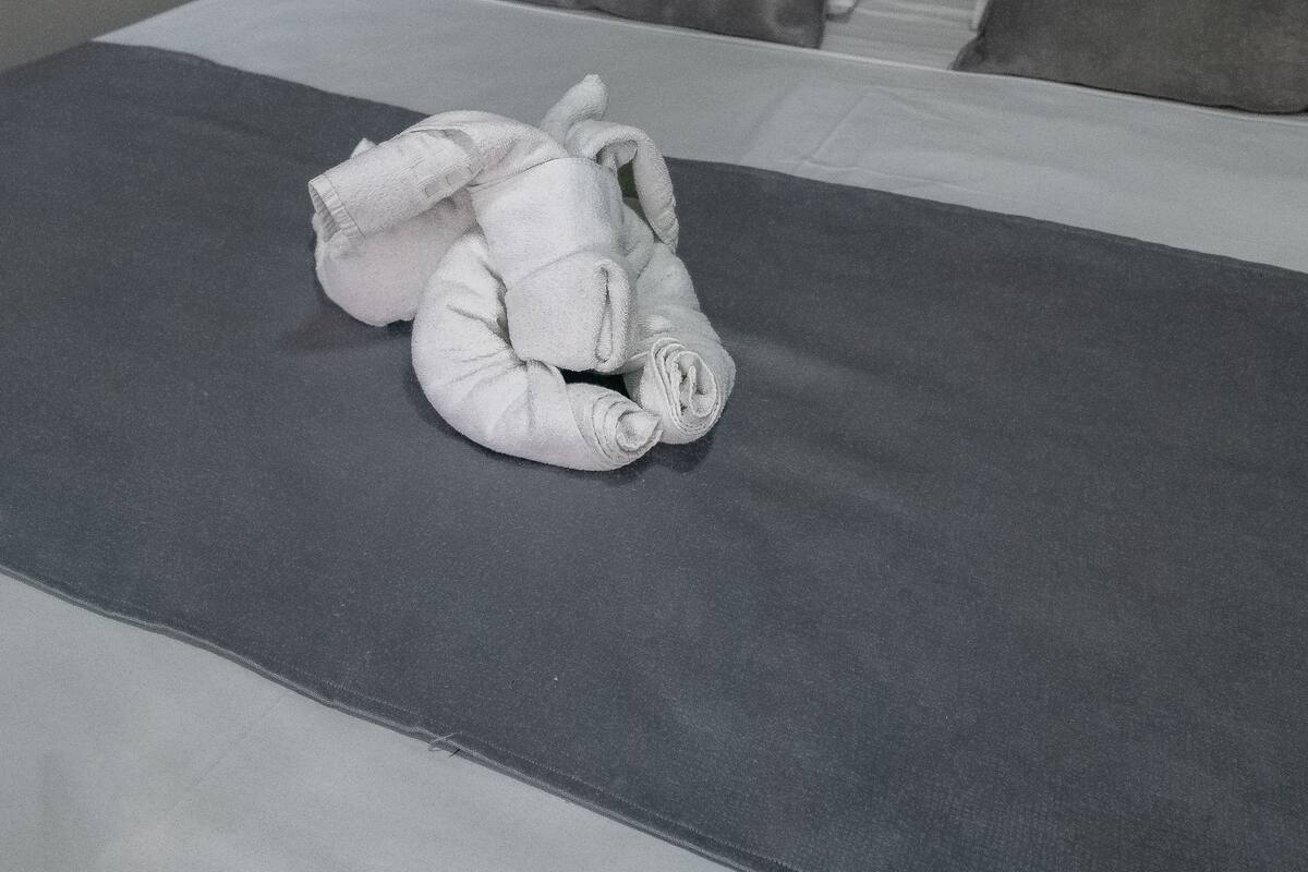 Una cama bien tendida con una manta gris y almohadas, un cabecero de madera y una pared verde.