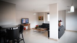 A modern living room with a dining area, a sofa, a coffee table, and a TV. - Blu Terrace Hotel (Blumenau)