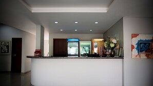 A hotel reception area with a curved counter, a refrigerator, and a wall-mounted art piece. - Blu Terrace Hotel (Blumenau)