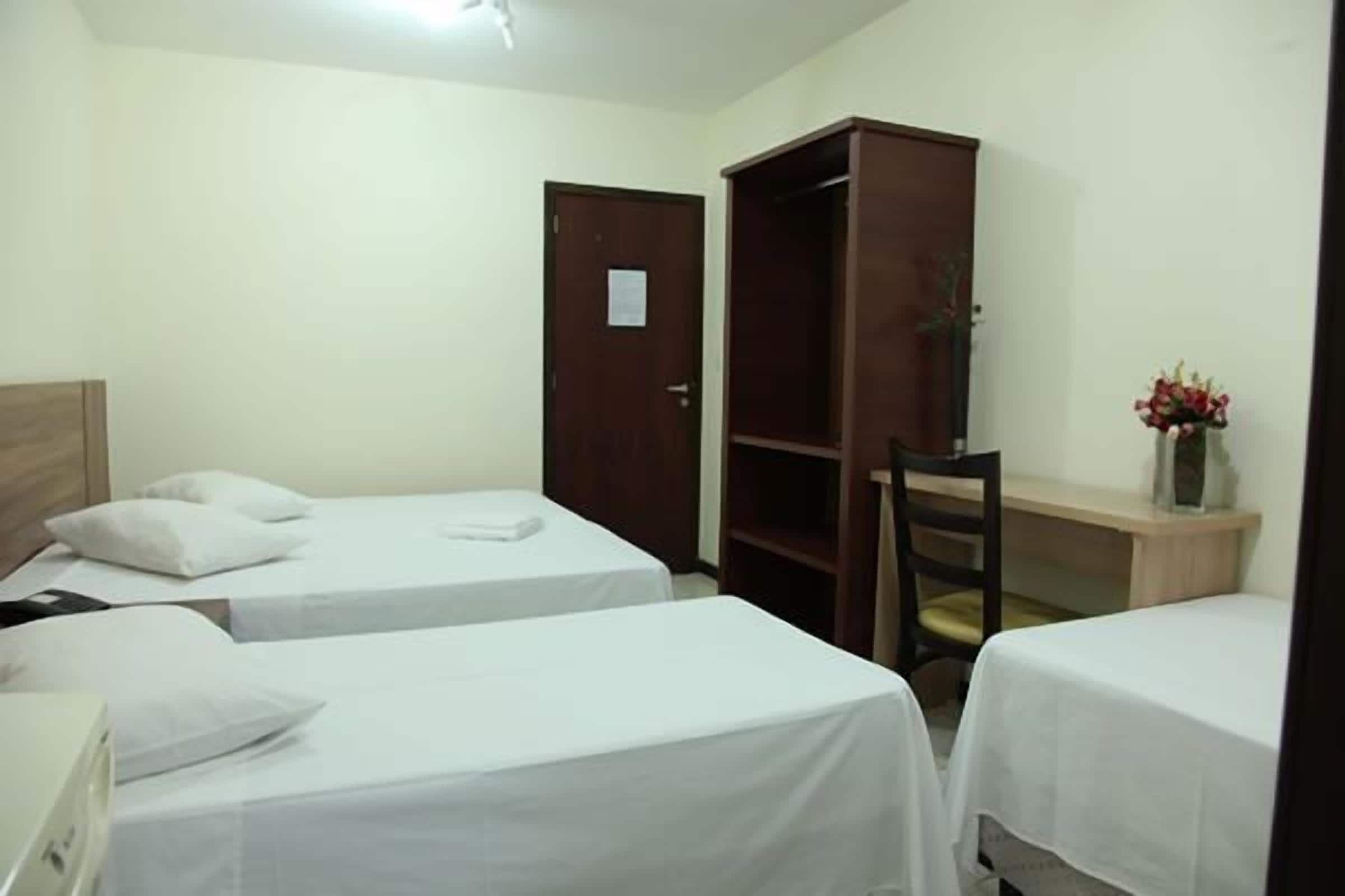 A hotel room with two single beds, a wooden wardrobe, a desk, and a chair.