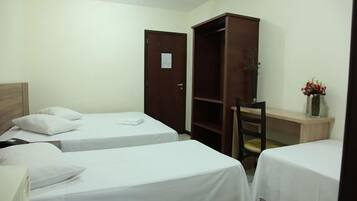 A hotel room with two single beds, a wooden wardrobe, a desk, and a chair.