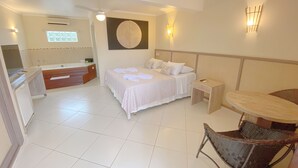 A hotel room with a bed, a small table, a chair, a bathroom with a bathtub, and a window.
