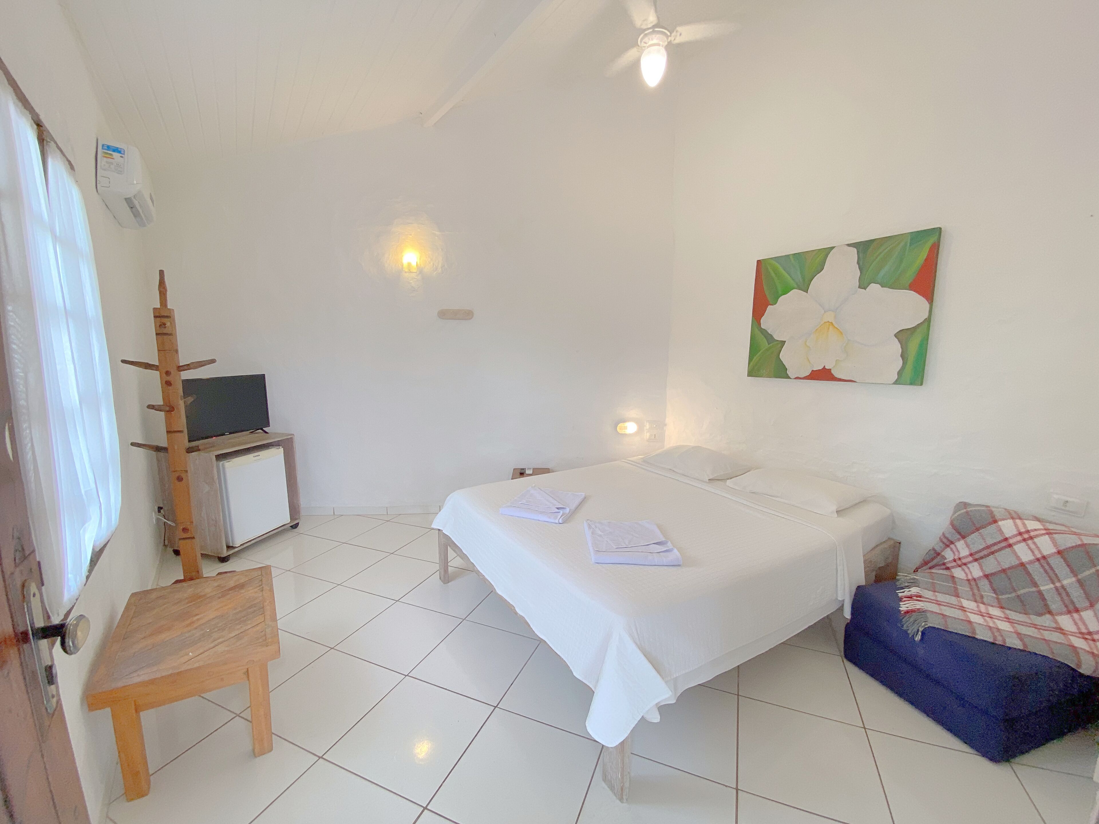 Ein Hotelzimmer mit Bett, kleinem Schreibtisch mit Fernseher, einem Sessel, einem Gemälde und einer blauen Couch.