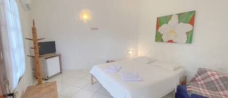 Ein Hotelzimmer mit Bett, kleinem Schreibtisch mit Fernseher, einem Sessel, einem Gemälde und einer blauen Couch.
