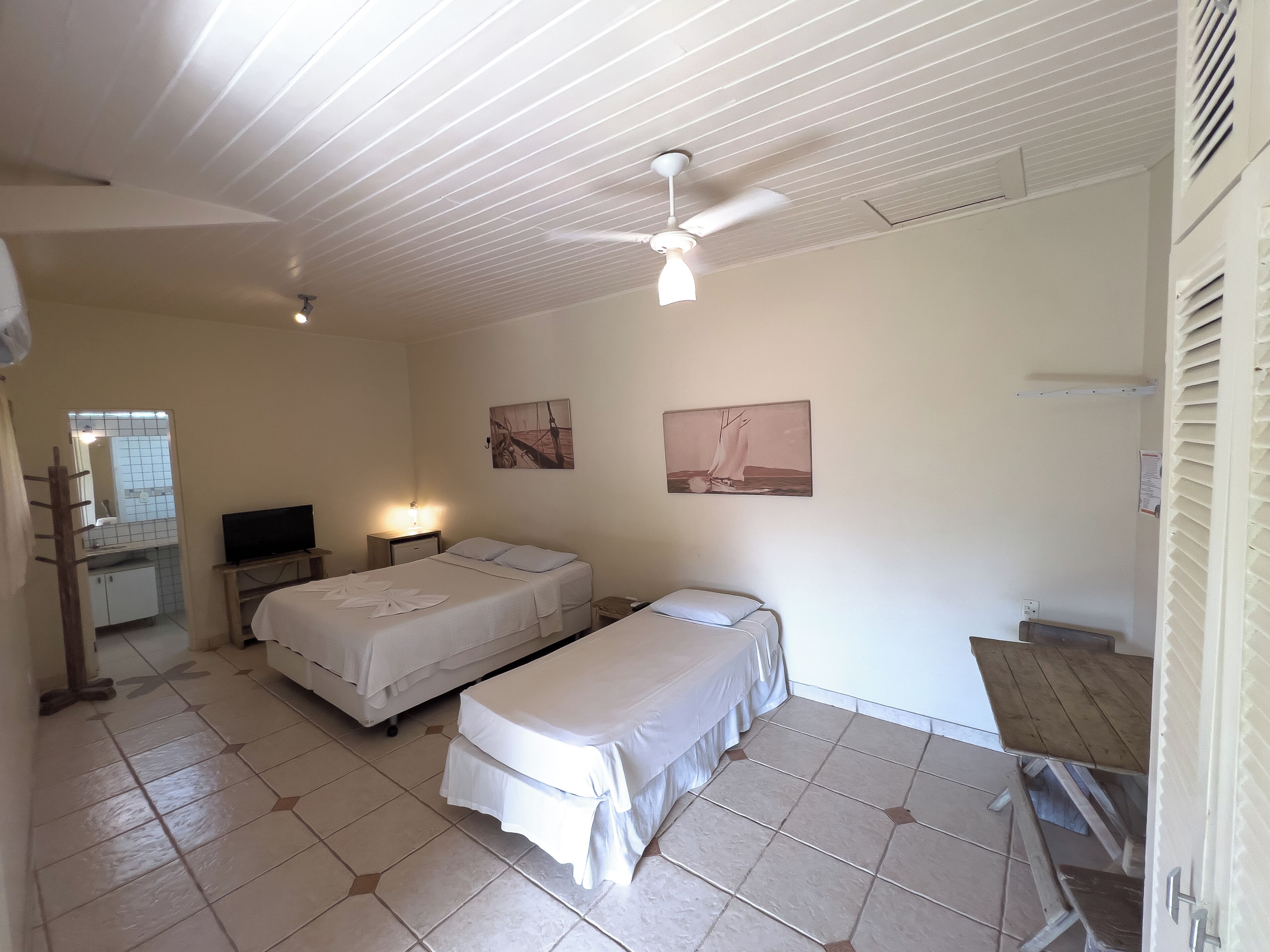 A room with two beds, a desk, a chair, a TV, and a ceiling fan.