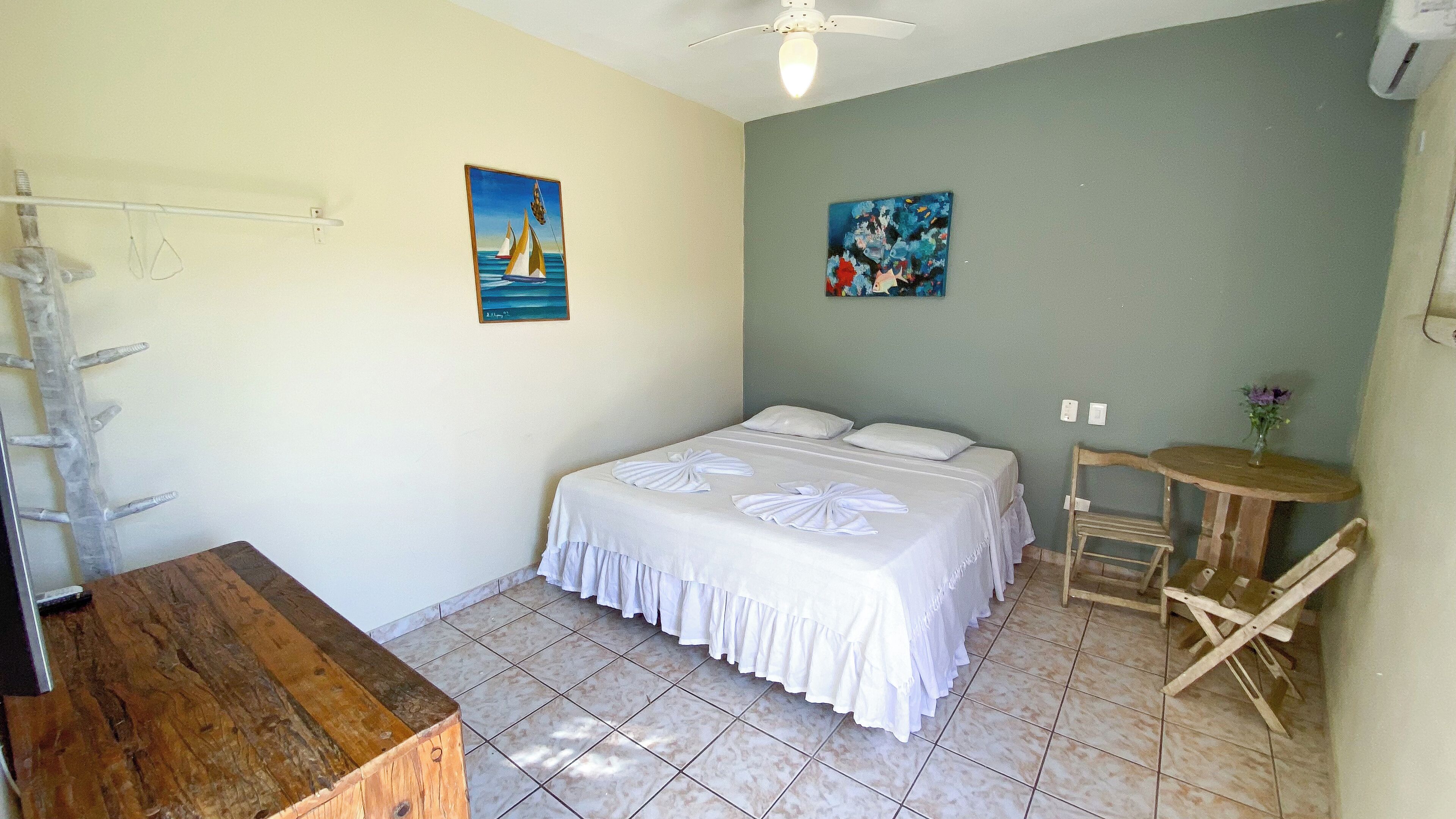 A bedroom with two beds, a wooden desk, a small table, and two paintings on the wall.