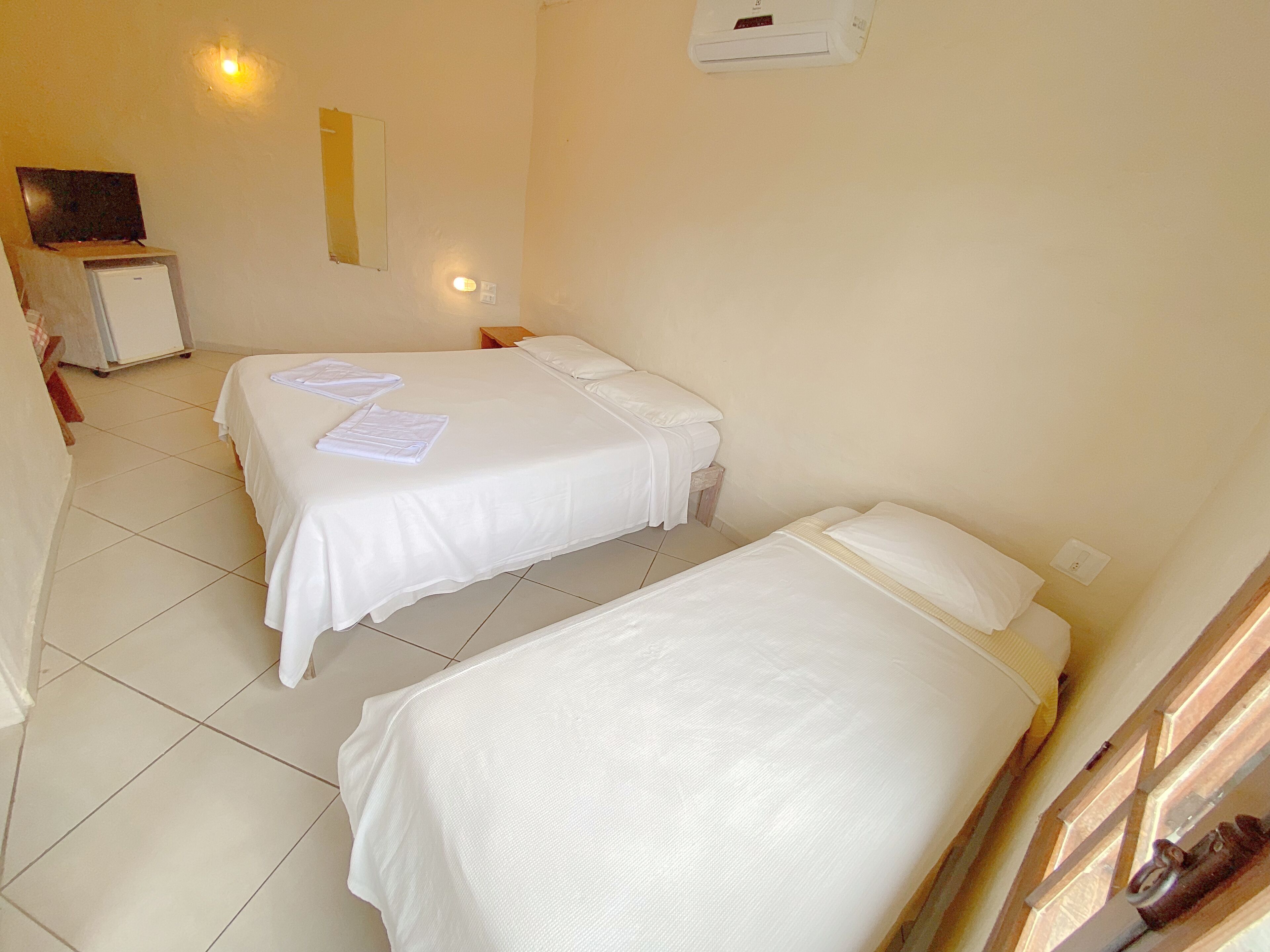 A hotel room with two beds, a small desk, and a wall-mounted air conditioner.