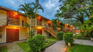 A two-story building with a wooden facade, a staircase leading to the upper level, and a well-maintained garden with palm trees and shrubs.