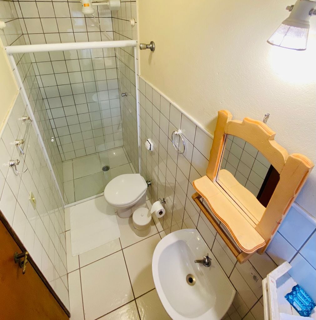 Un baño con cabina de ducha de vidrio, inodoro, lavamanos y tocador de madera con espejo.