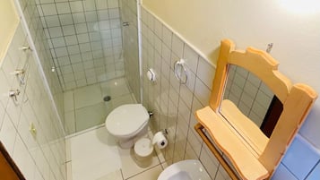 Un baño con cabina de ducha de vidrio, inodoro, lavamanos y tocador de madera con espejo.