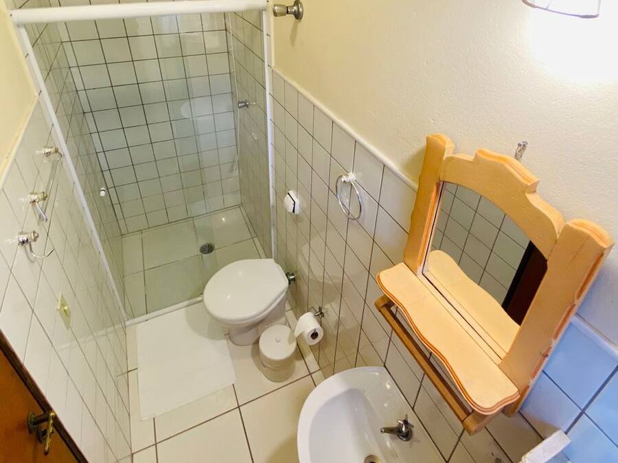 Un baño con cabina de ducha de vidrio, inodoro, lavamanos y tocador de madera con espejo.