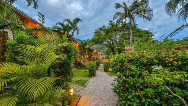 A pathway leading to a building with a staircase, surrounded by lush greenery and palm trees.