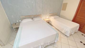 Une chambre d’hôtel avec deux lits simples, une table de chevet avec une lampe, une porte en bois et un sol carrelé.
