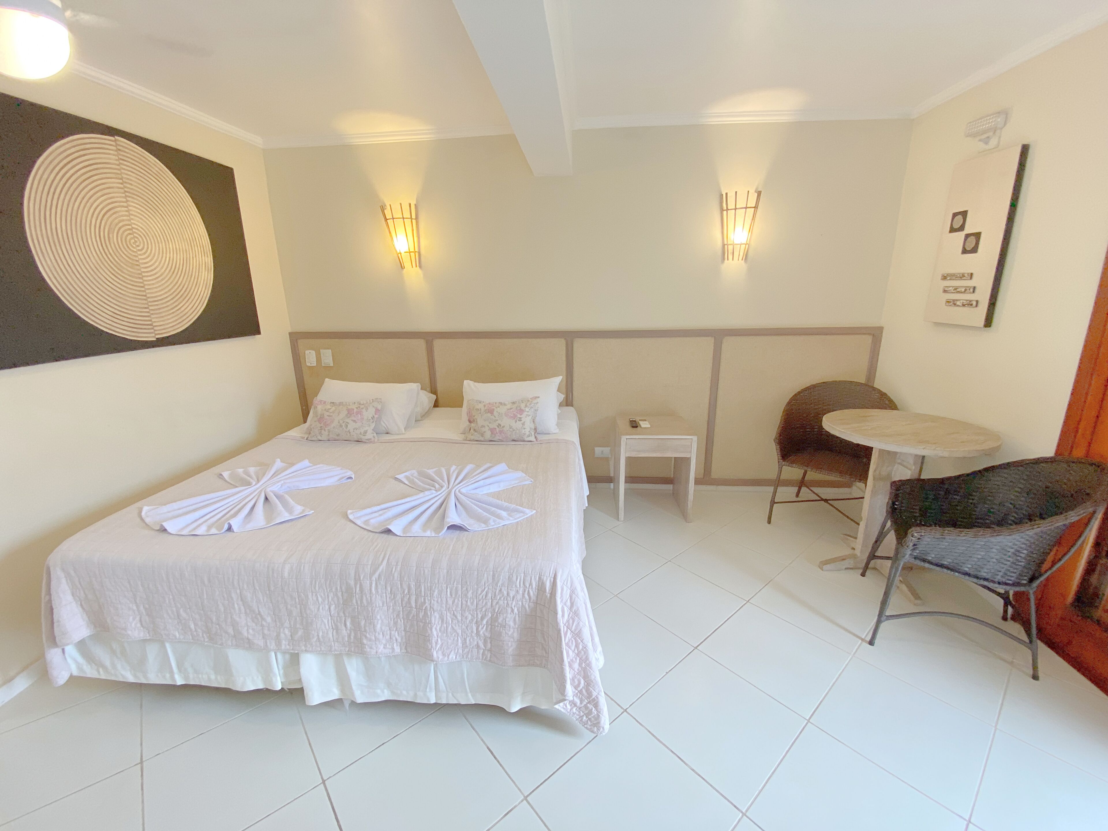 Una habitación de hotel con una cama grande, dos mesitas de noche, una silla y una pequeña mesa.
