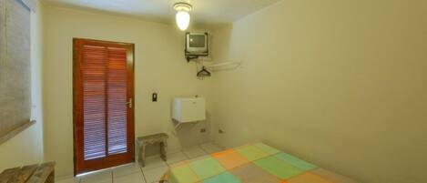 Una habitación pequeña y sencilla con una cama, un banco de madera, un inodoro y un televisor montado en la pared.