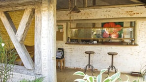 A rustic bar area with wooden beams, a thatched roof, and a bar counter with stools.