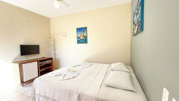 A bedroom with a bed, a TV, a drying rack, and a painting on the wall.