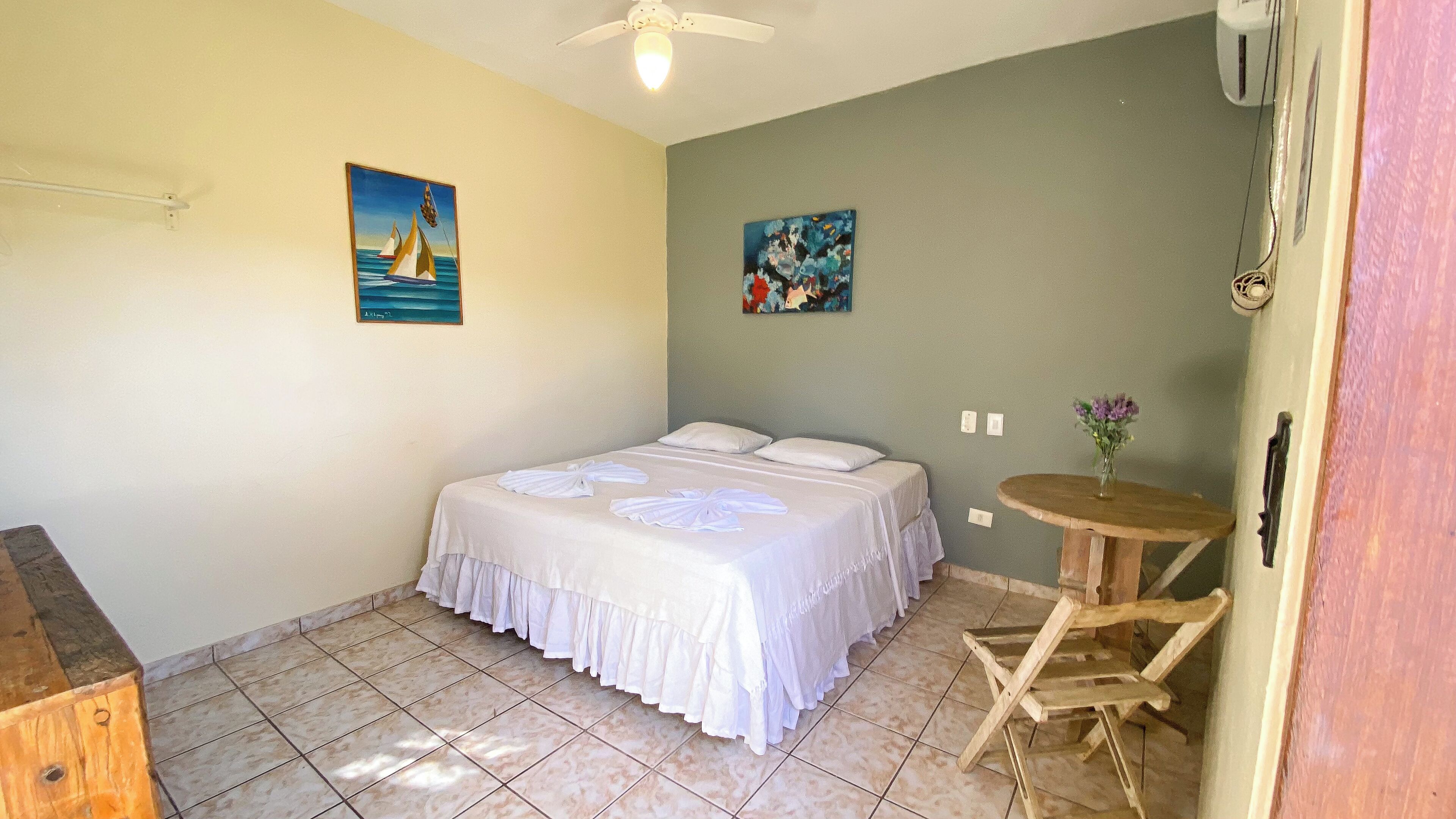 A bedroom with a bed, a small round table, and two paintings on the walls.