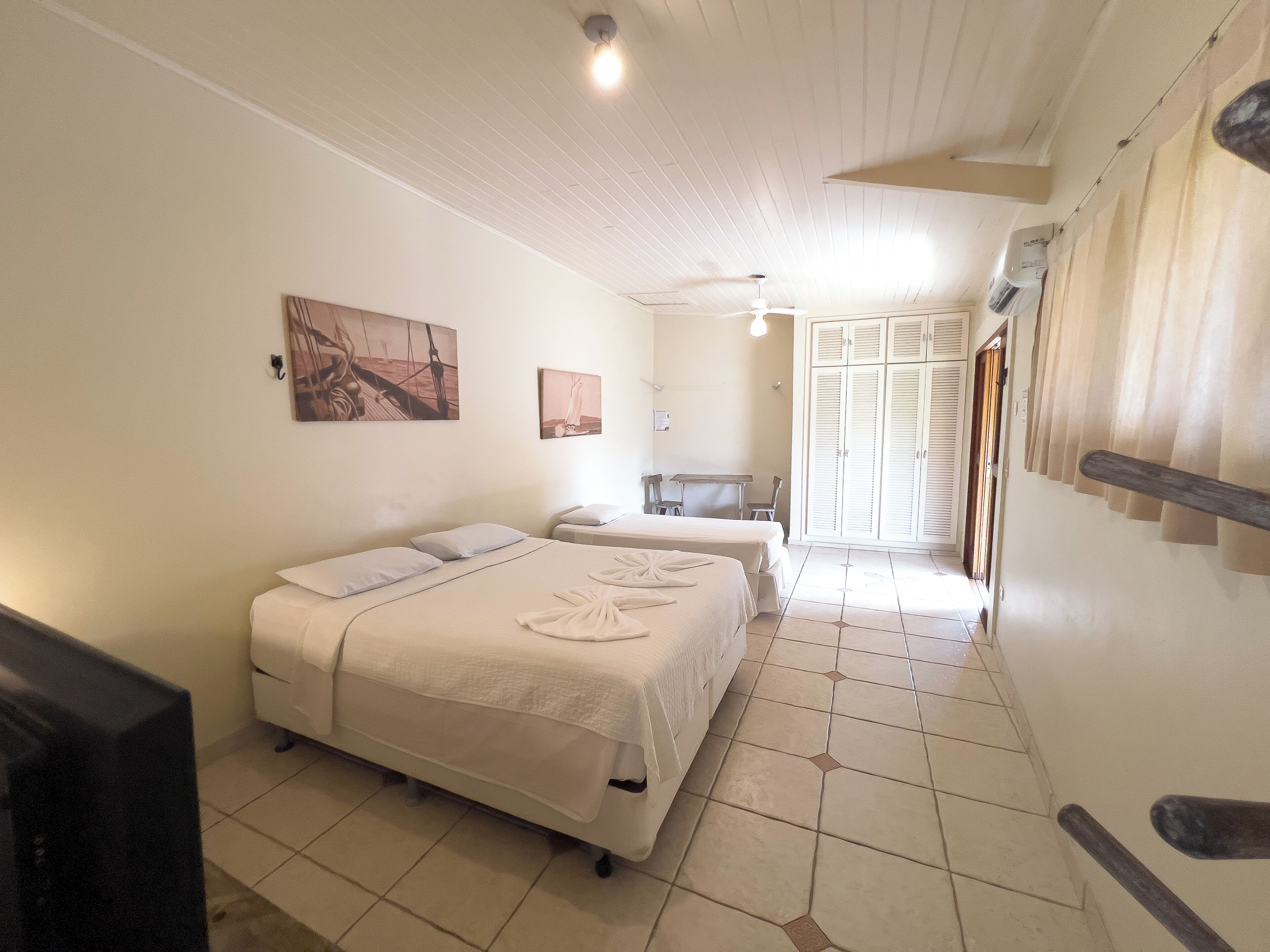 Ein Hotelzimmer mit Bett, Schreibtisch und Stuhl. Es gibt einen Kleiderschrank und ein Fenster mit Vorhängen.